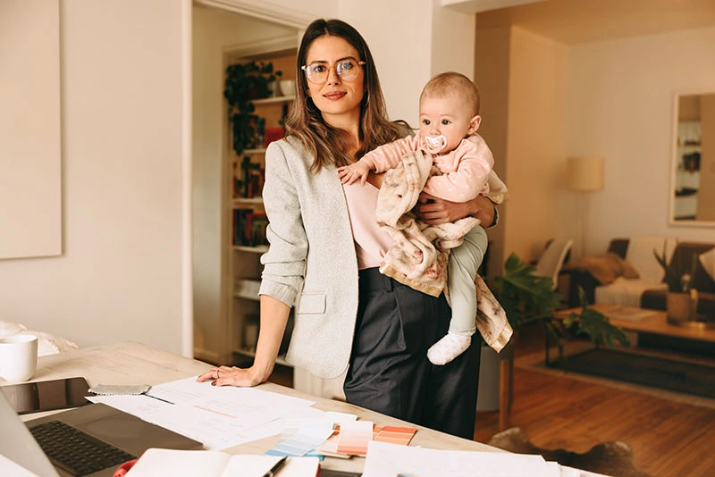 Femme d'affaires tenant son bébé debout dans son bureau à domicile